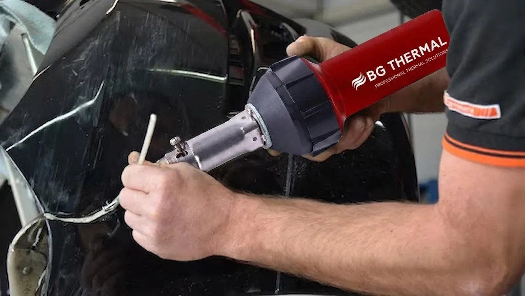 An auto body technician using a red BG THERMAL heat gun with a specialized nozzle to weld and repair a cracked black plastic car bumper